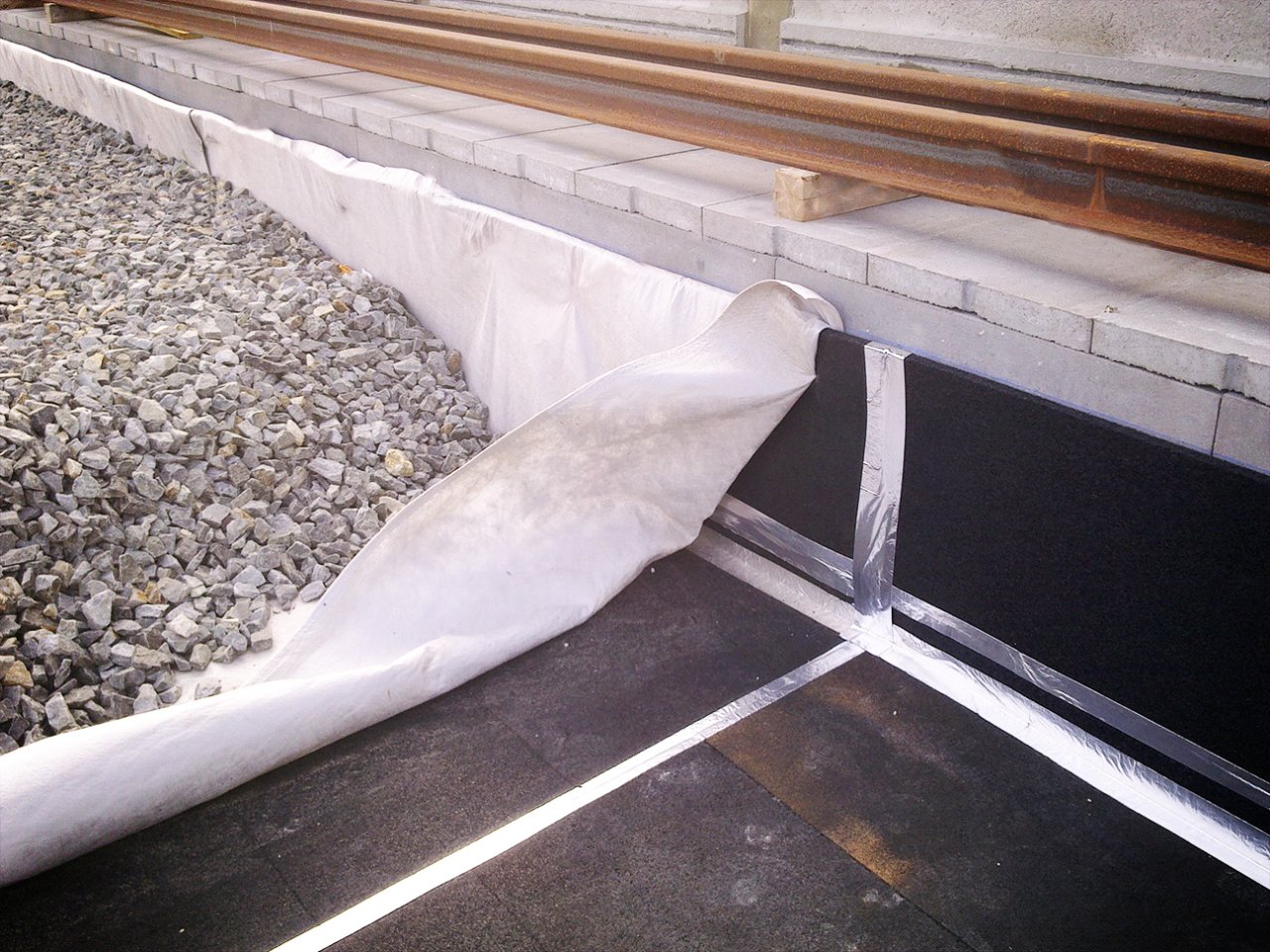 Billede afmMåtter lavet af et vibrationsdæmpende materiale lagt ud under ballasten, mens man installerer en ny skinne til tog.